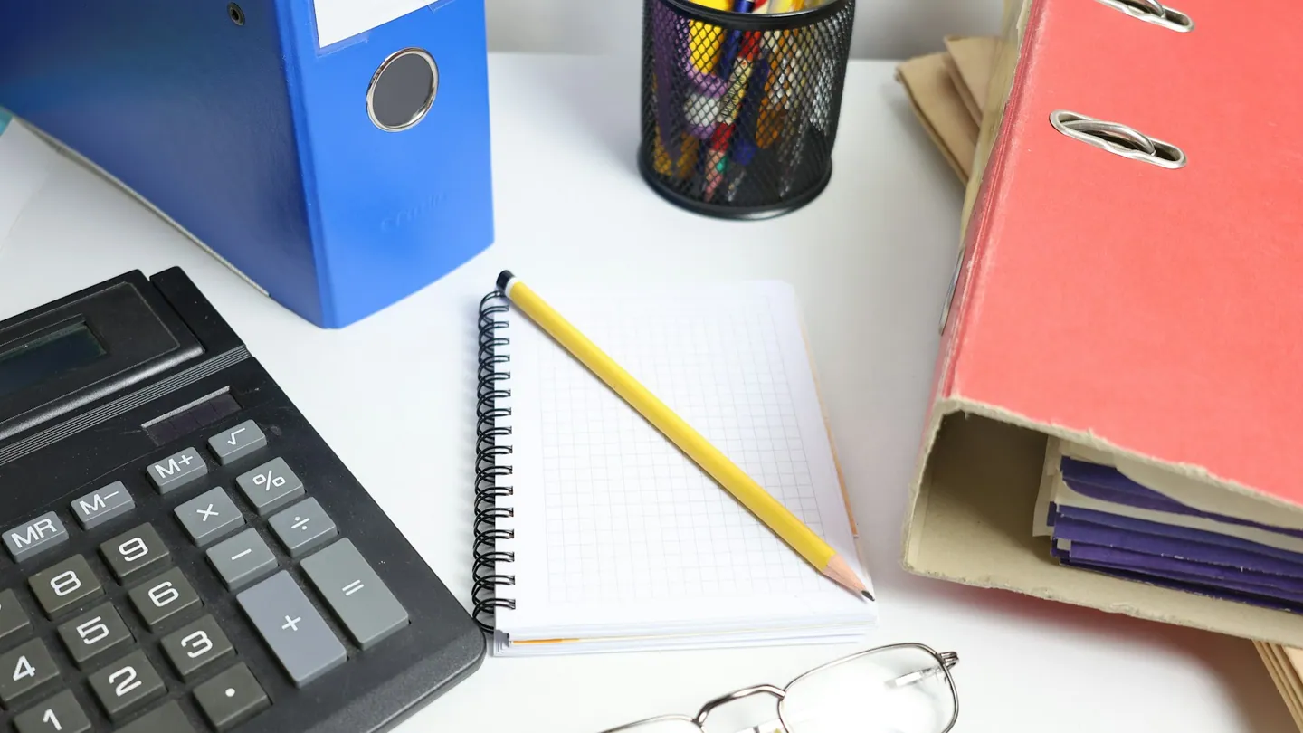 Una mesa con archivadores, calculadora y cuaderno.